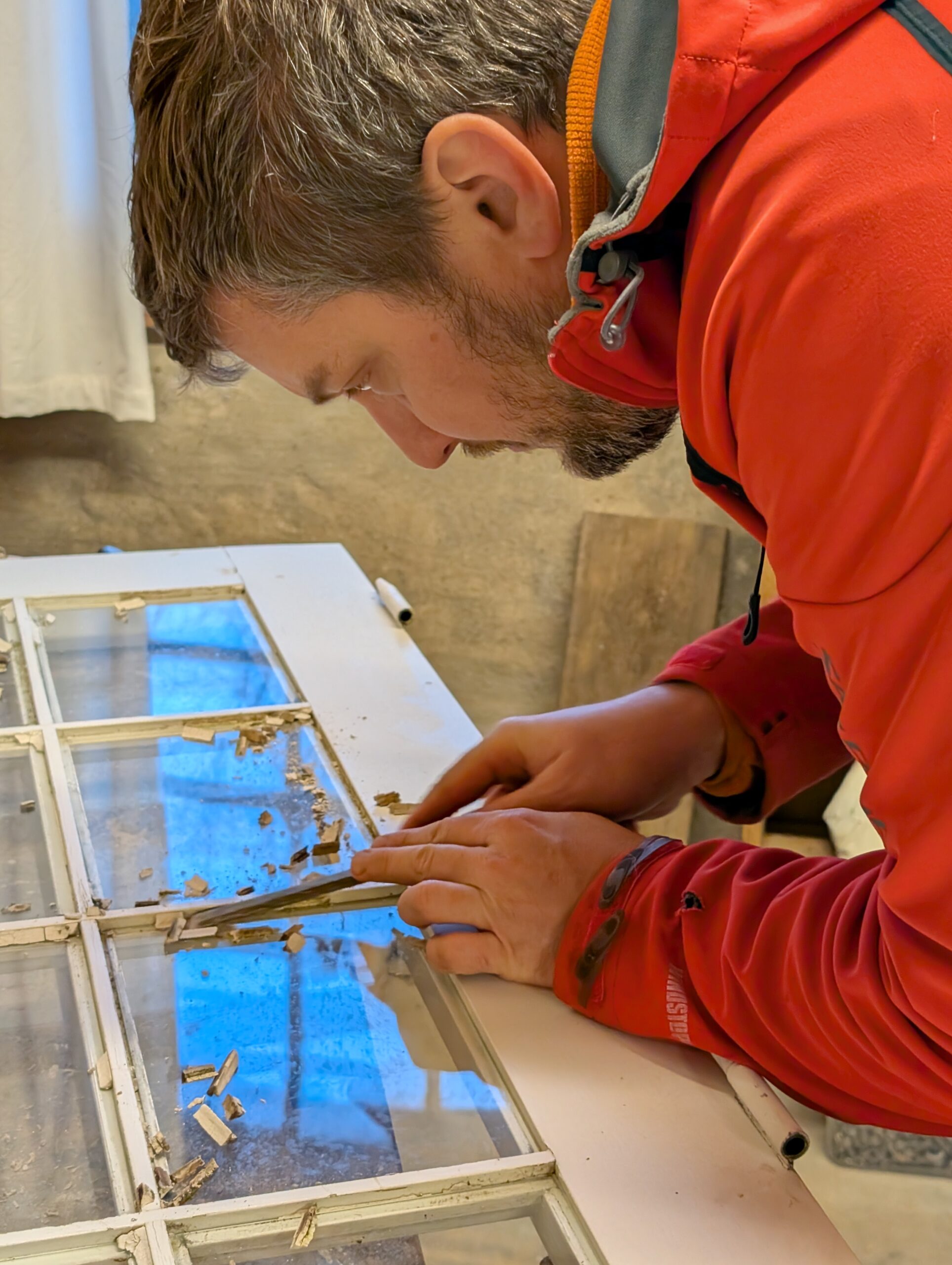 Man in a red jacket restoring an old window frame during a work day at the homestead