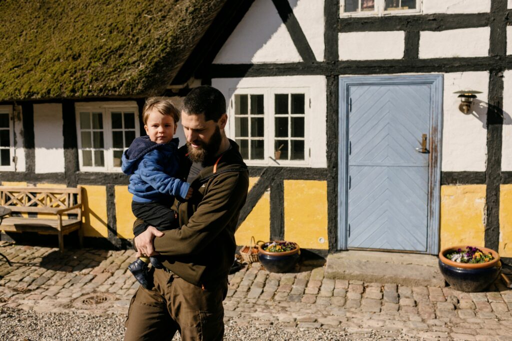 Father holding his young son in front of a thatched, half-timbered Danish farmhouse